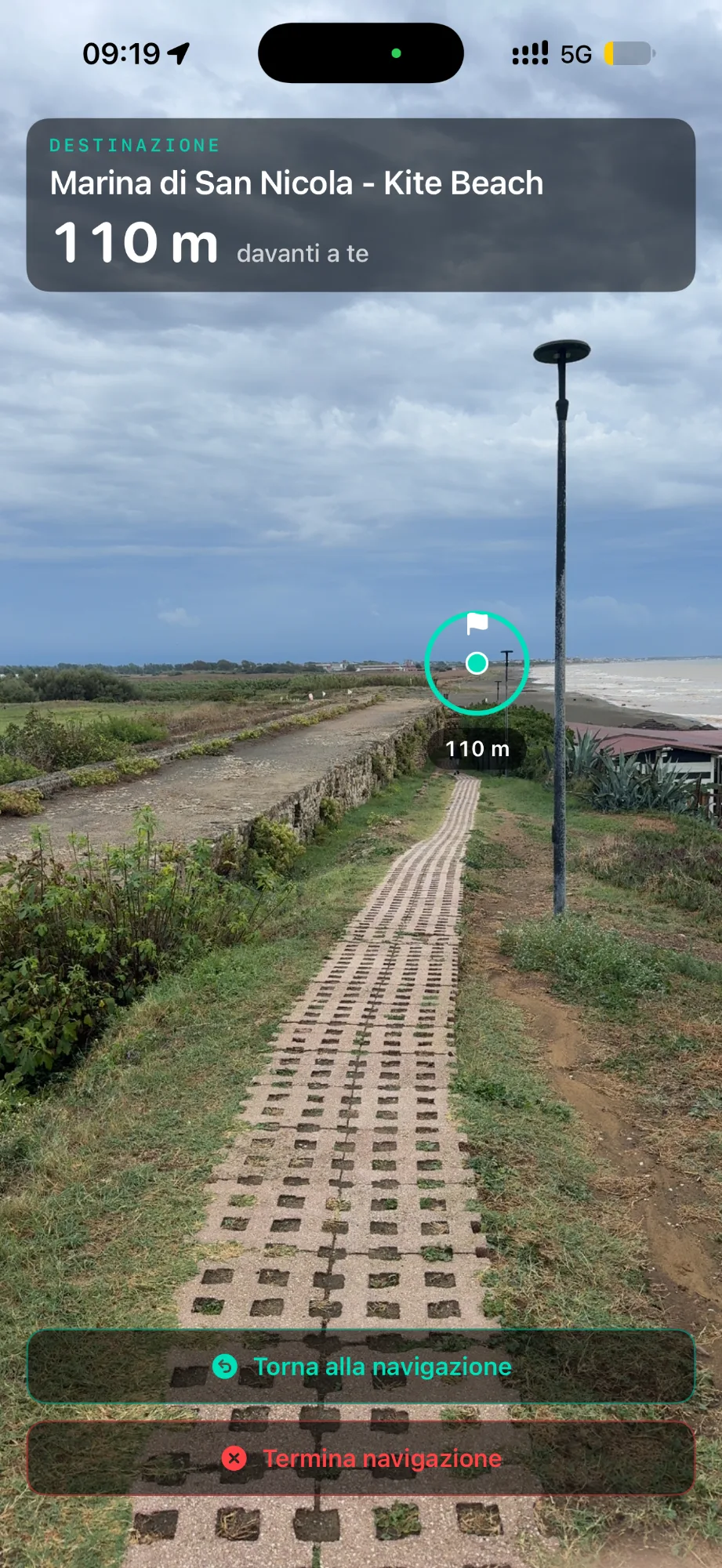 Waypoint Navigation AR in GeoFix: in alto la destinazione della navigazione in corso, con nome e distanza; nella scena un indicatore la segna sul sentiero davanti
